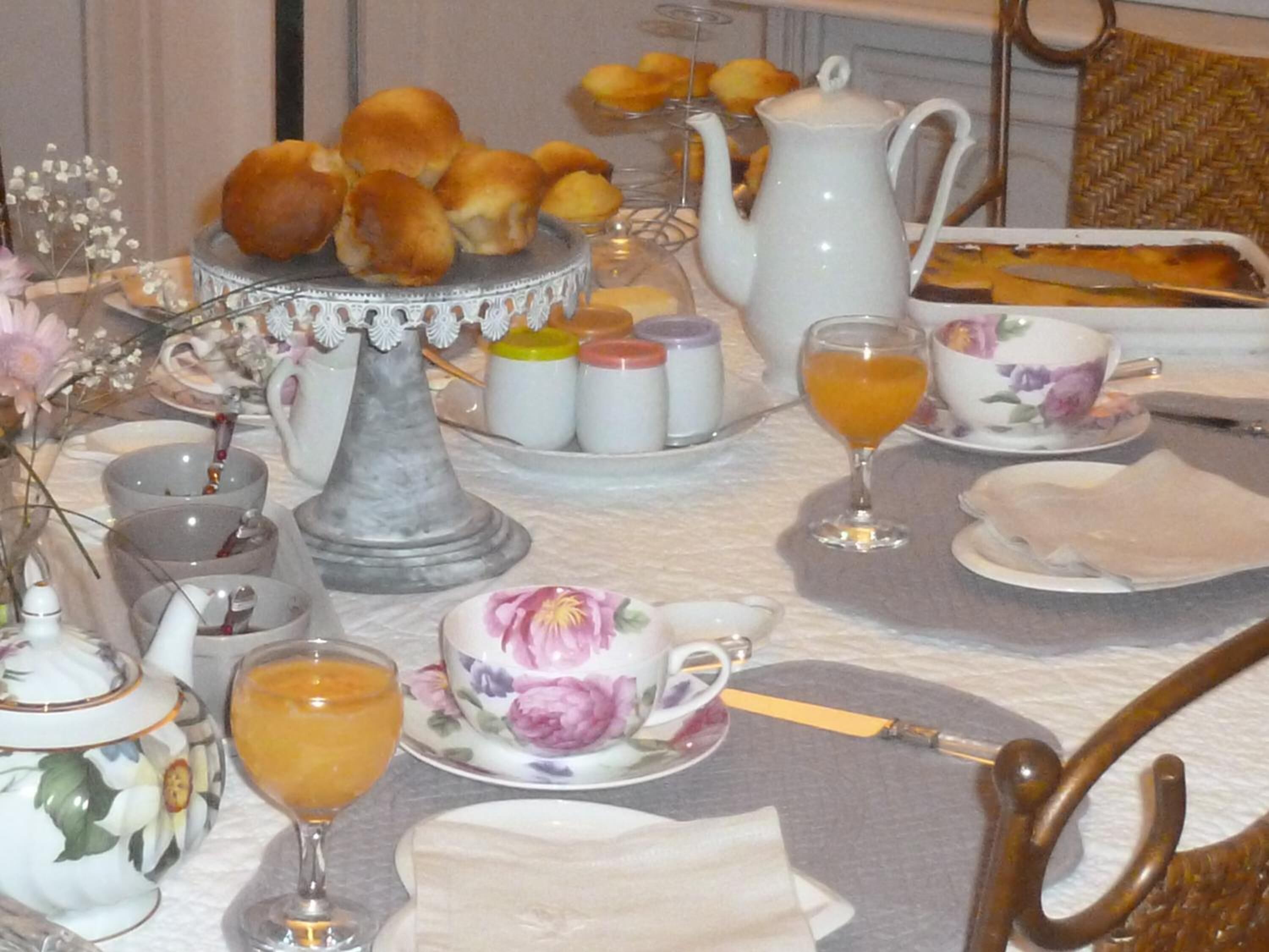 A breakfast table with tea cups, a teapot, a pitcher, and a plate of pastries.