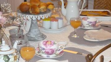 A breakfast table with tea cups, a teapot, a pitcher, and a plate of pastries.