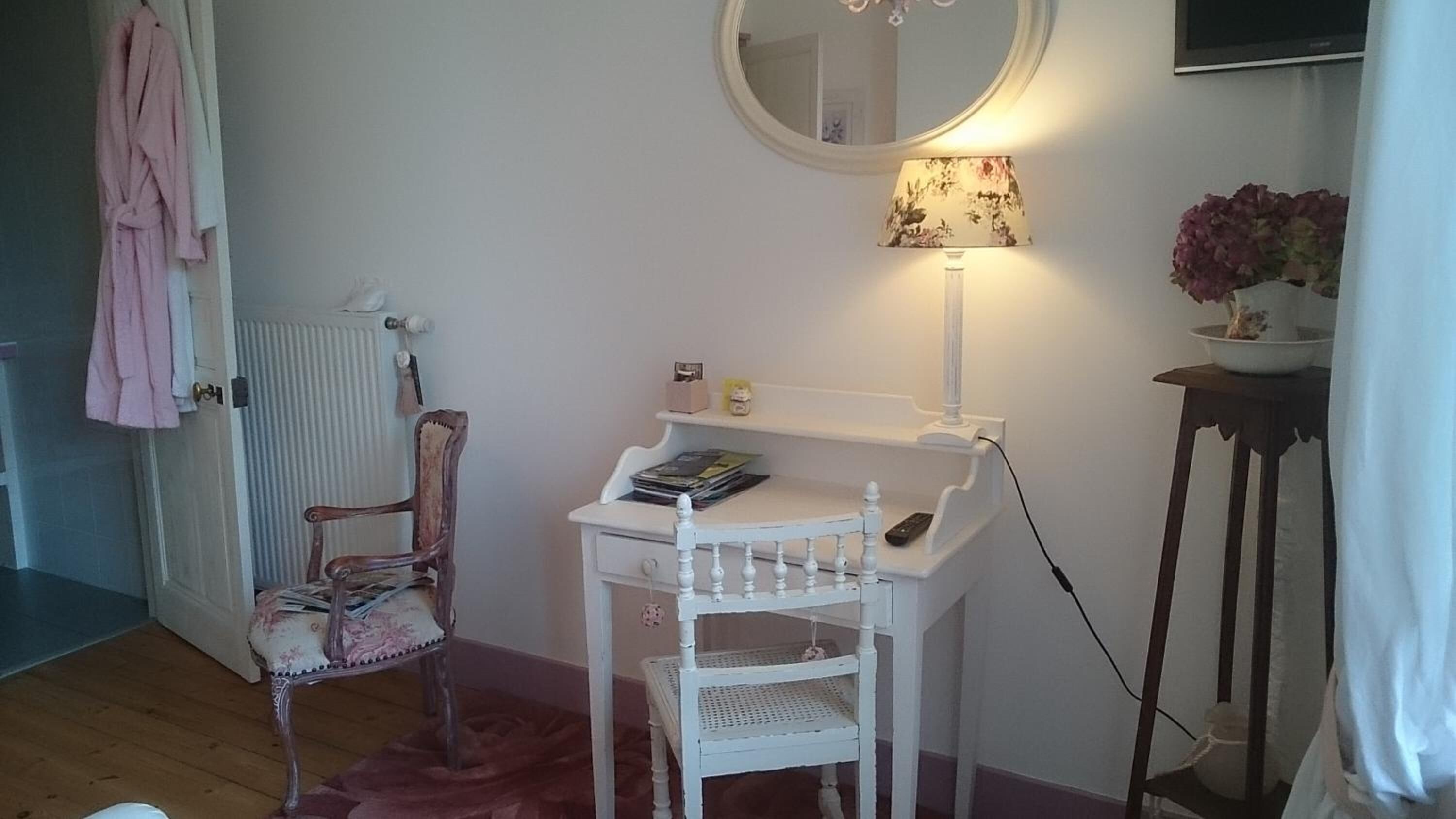 Une salle de bain avec un meuble-lavabo blanc, un miroir, une lampe, une chaise et un radiateur.