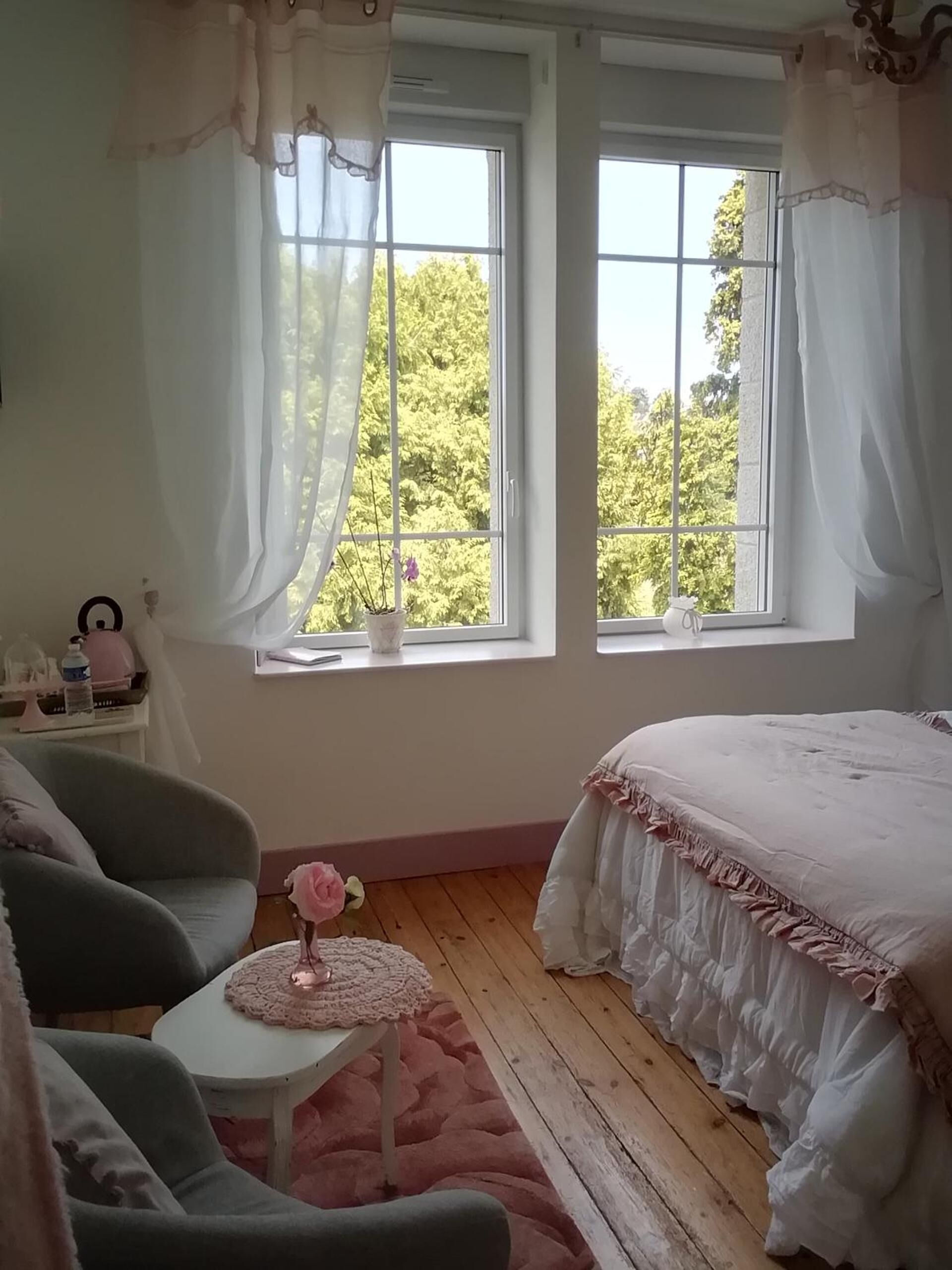 Un dormitorio con una cama, una silla, una mesita y una ventana con cortinas.