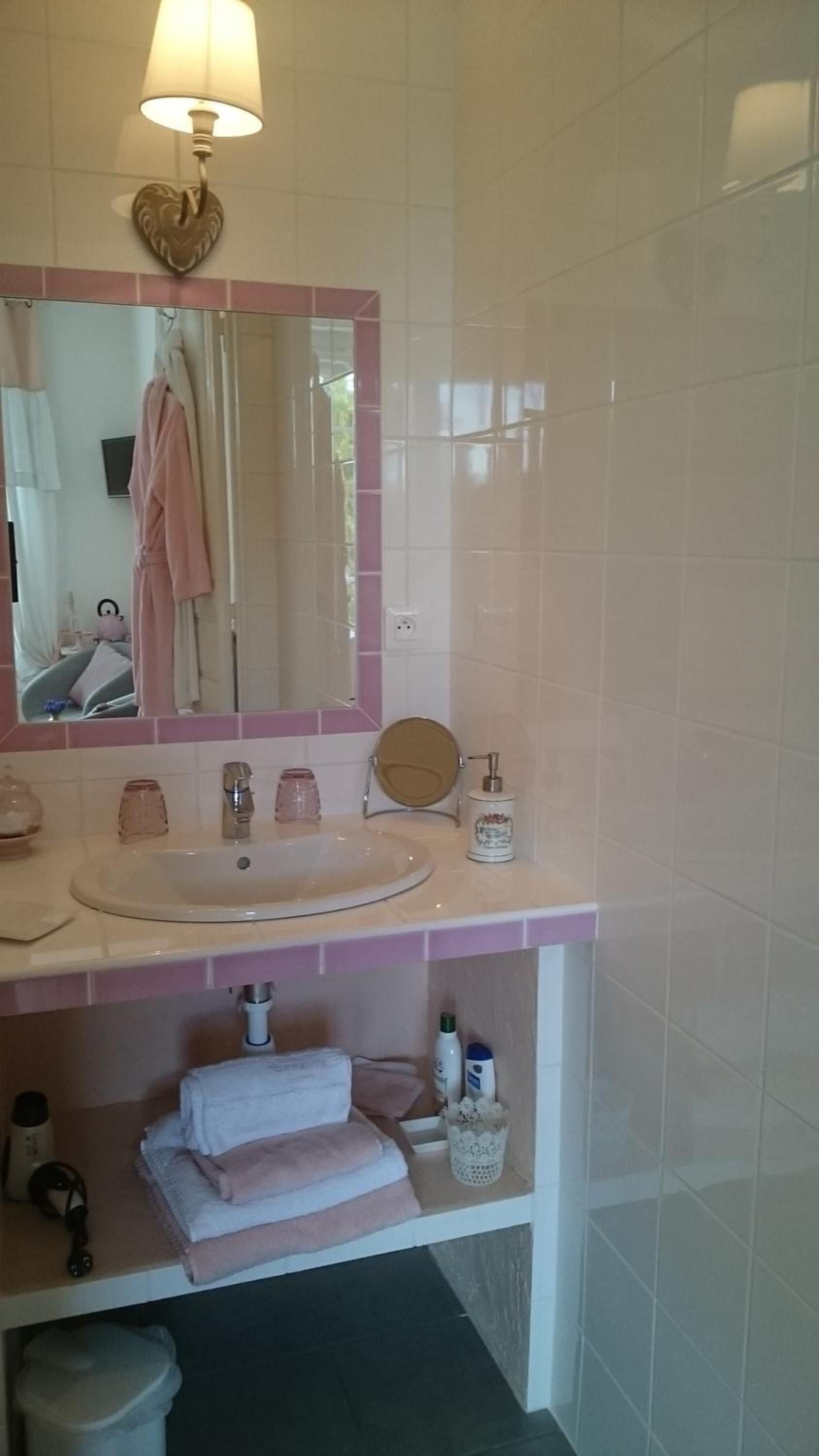 Un baño con tocador rosa, un espejo redondo, un inodoro y un lavabo con dispensador de jabón.