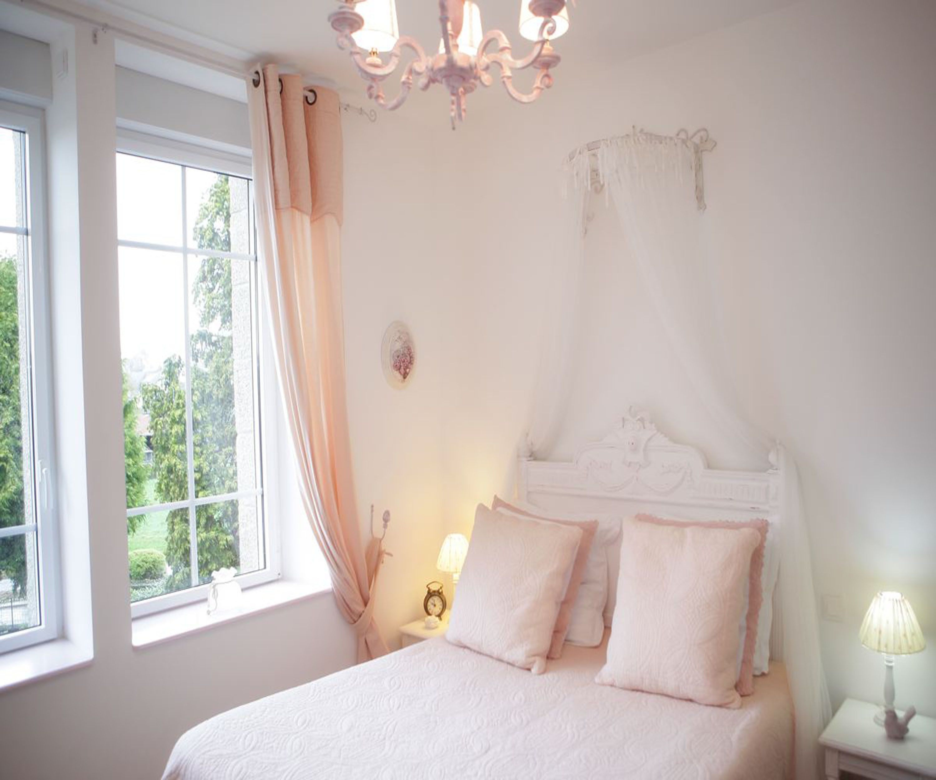 A bedroom with a canopy bed, a bedside table with a lamp, and a window with curtains.