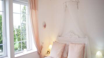 A bedroom with a canopy bed, a bedside table with a lamp, and a window with curtains.