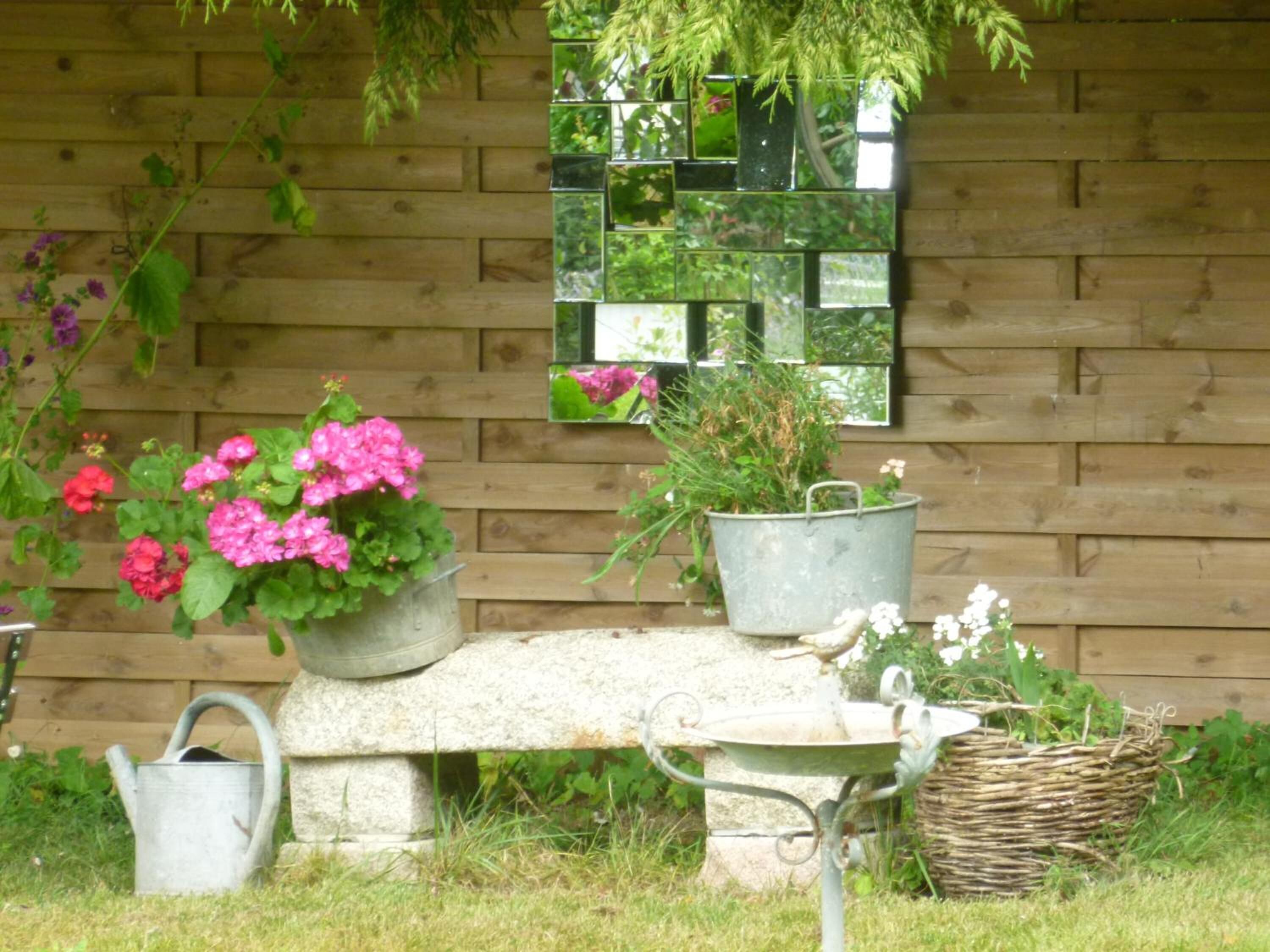 A garden with a wooden wall, a stone bench, and various potted plants.