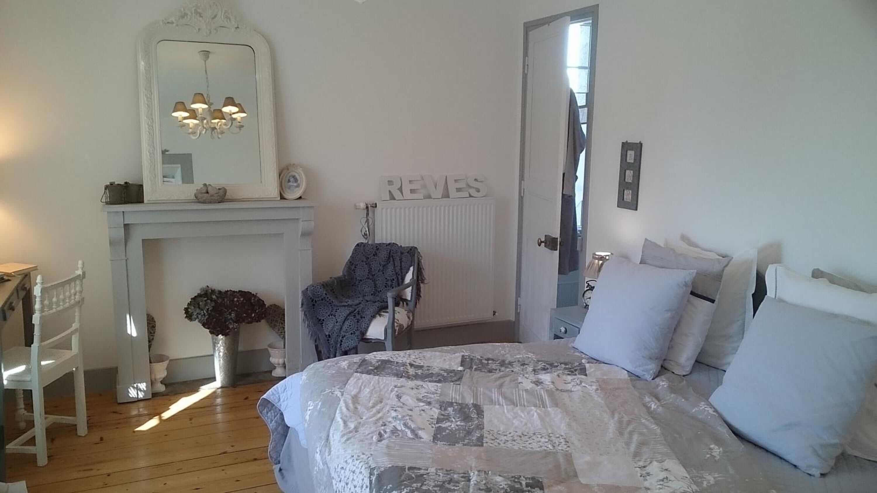 A bedroom with a bed, a chair, a dresser, a mirror, and a fireplace.
