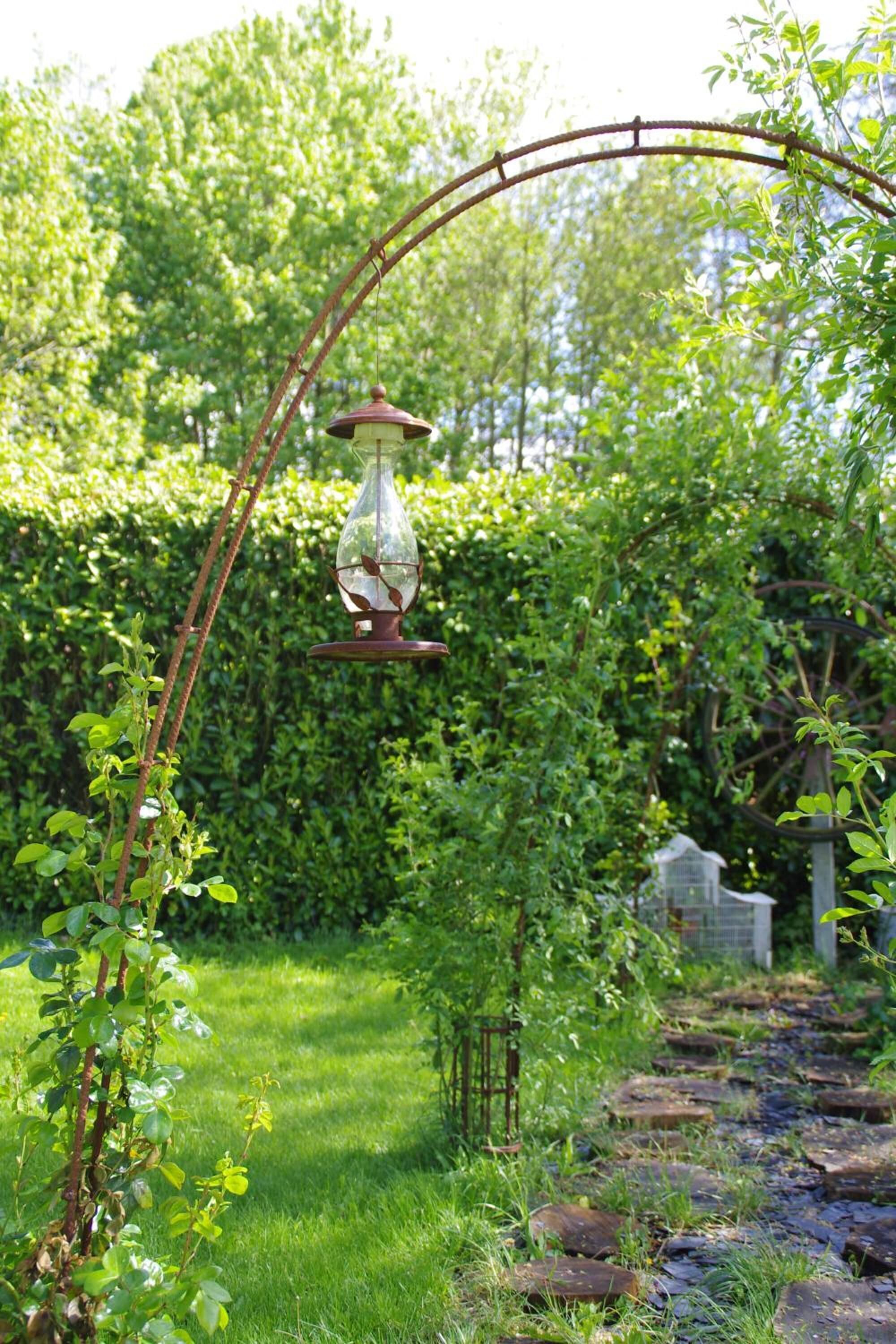 Een tuin met een rustieke metalen boog en een hanglamp.
