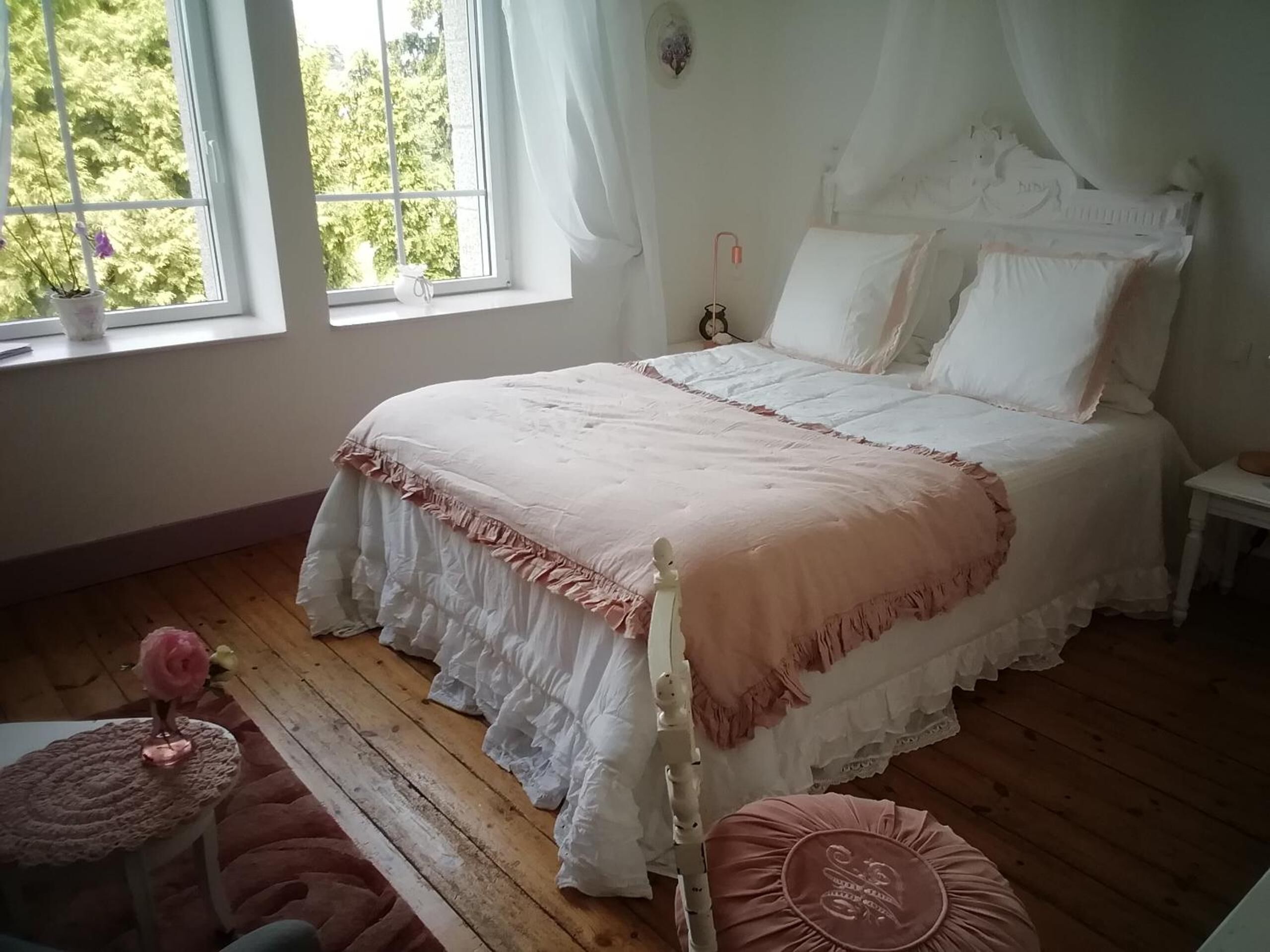Une chambre avec un grand lit, une table de chevet, une commode, une fenêtre avec des rideaux et une vue sur la verdure à l’extérieur.