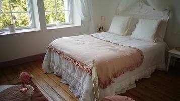Une chambre avec un grand lit, une table de chevet, une commode, une fenêtre avec des rideaux et une vue sur la verdure à l’extérieur.