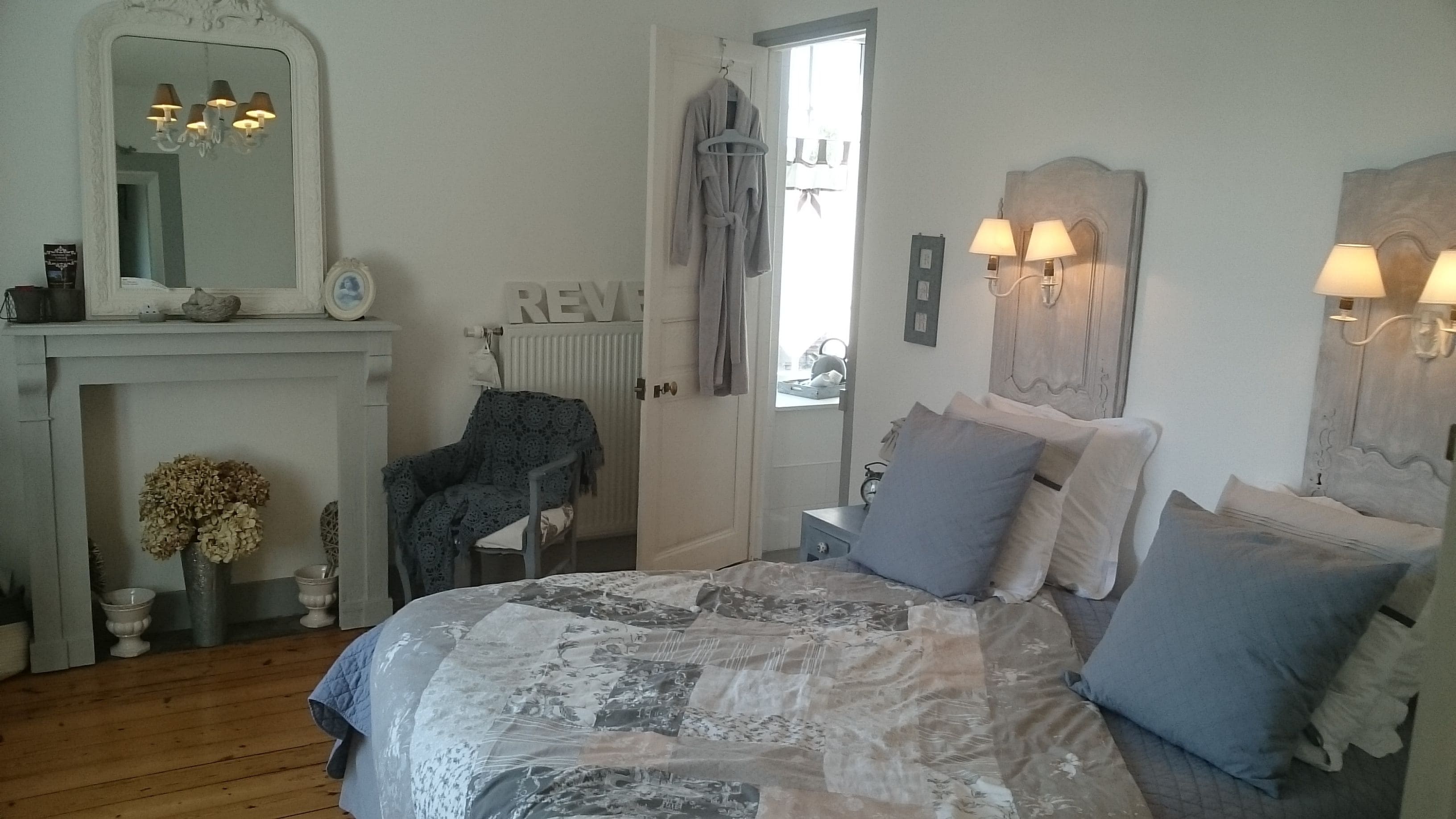 A bedroom with a bed, a chair, a dresser, a mirror, and a fireplace.