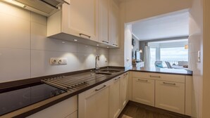 Una cocina moderna con armarios blancos, encimera negra y vista al mar a través de una ventana.