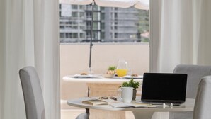 A balcony with a table set for breakfast, including a laptop, a mug, and a book.