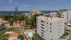 A modern apartment complex with a rooftop pool, surrounded by greenery and a view of the sea.