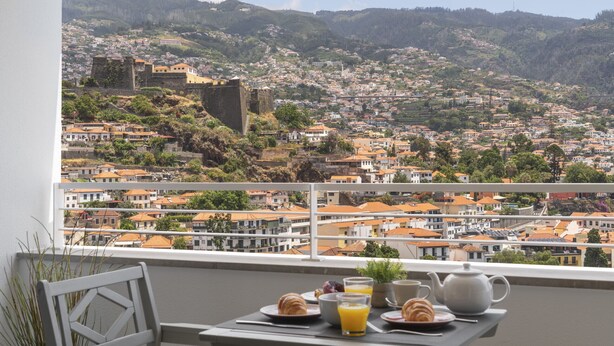 A balcony with a table set for breakfast, overlooking a town with historic buildings and a hill.