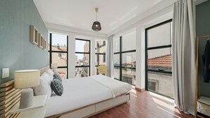 A modern bedroom with a large bed, bedside tables, and a view of the city through large windows. - Pelourinho III, studio in Funchal (Funchal)