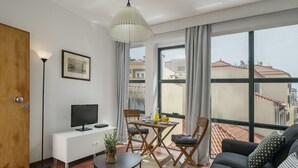 A modern living room with a sofa, a TV on a white cabinet, a dining table with chairs, and a large window with a city view. - Pelourinho III, studio in Funchal (Funchal)