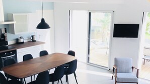 Moderni keittiö, jossa on ruokailutila, seinälle asennettu televisio ja liukuovi, joka johtaa ulkotiloihin.