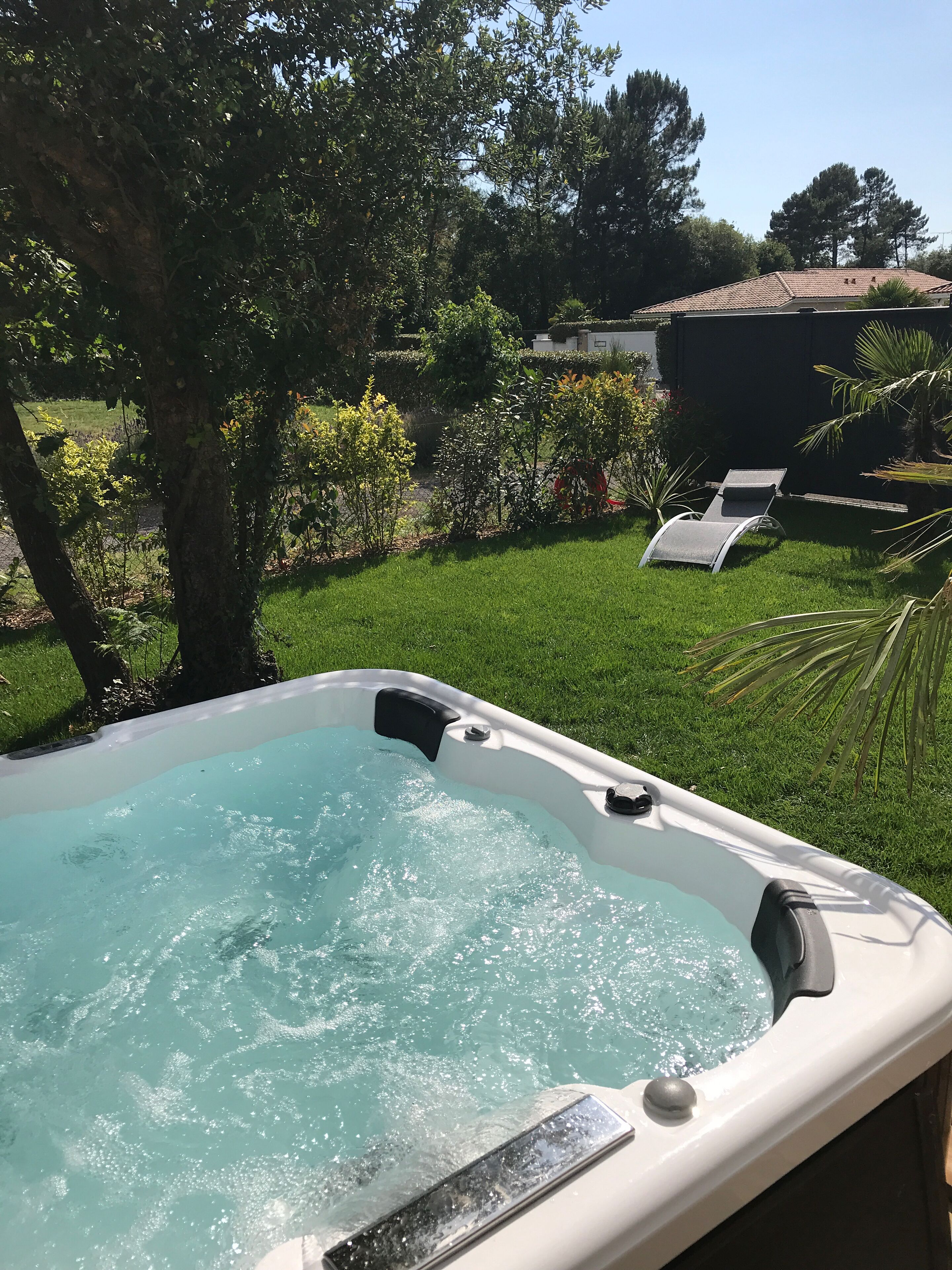 A hot tub in a backyard with a lawn, trees, and a chair.