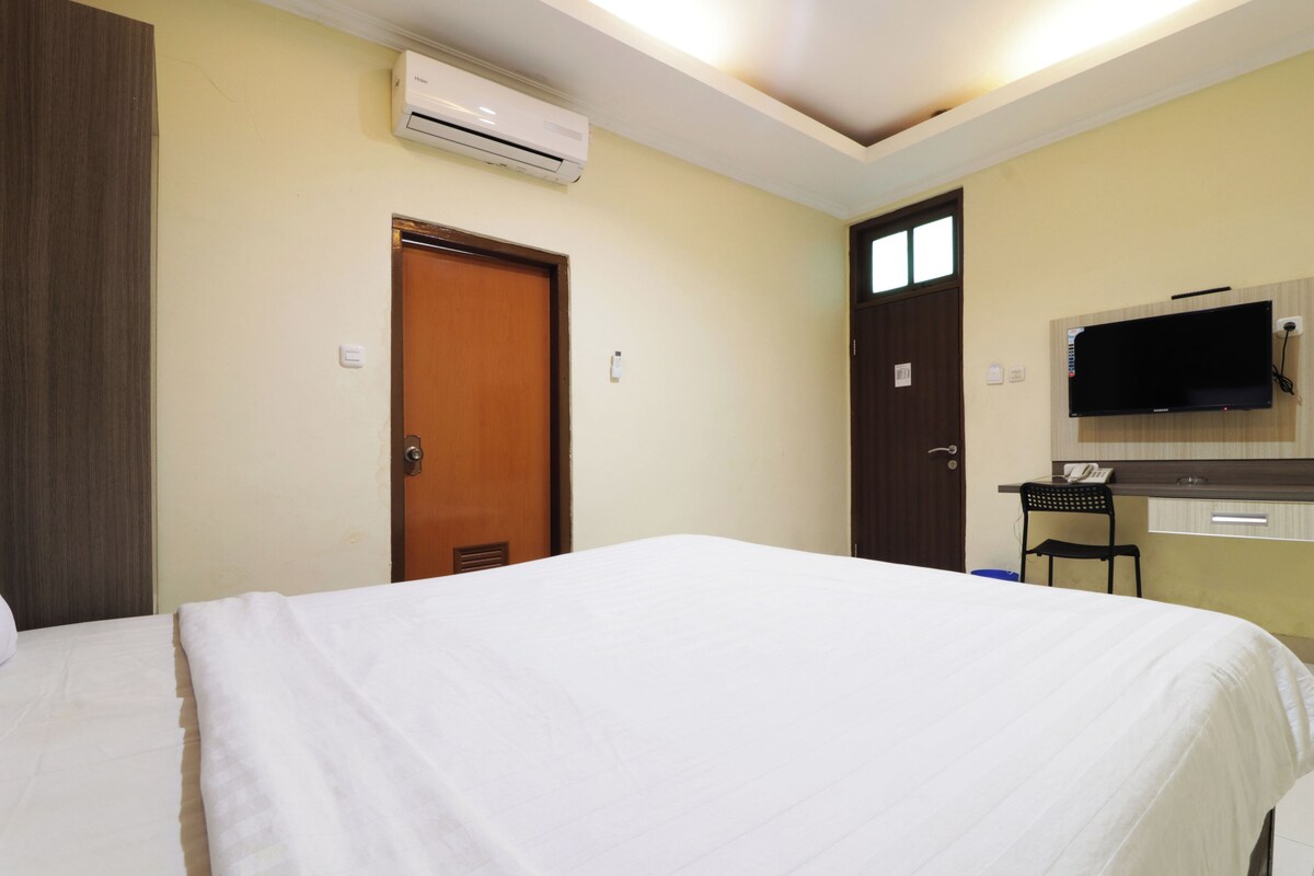 A hotel room with a bed, a desk with a chair, an air conditioner, and a television mounted on the wall.