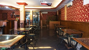 Een restaurantinterieur met houten tafels en stoelen, behang met een patroon en een plafond met inbouwspots.