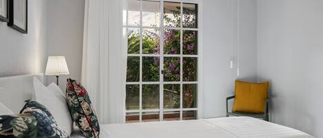 A hotel room with a bed, a window with a view of greenery, a lamp, and a chair.