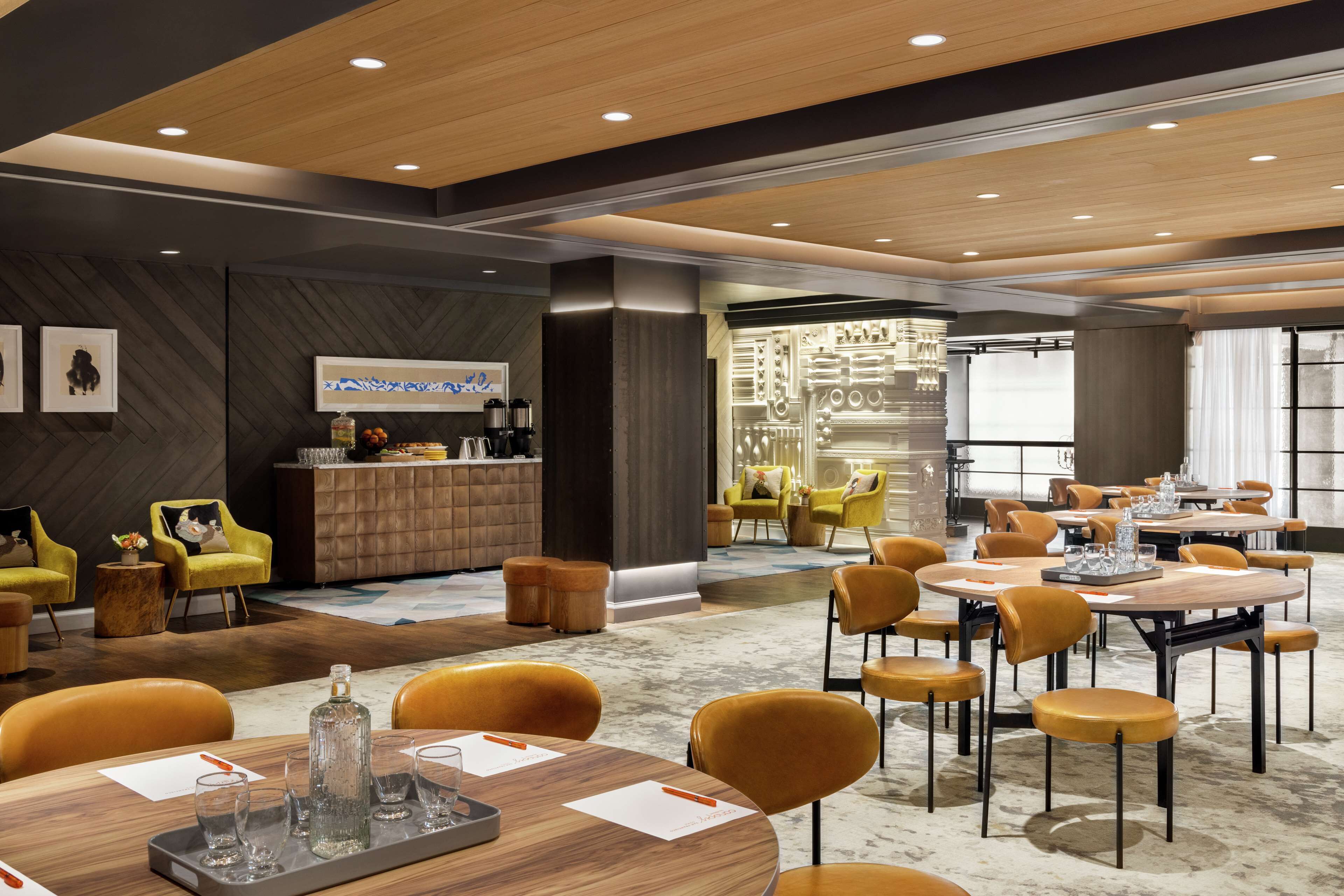 A modern hotel lobby with round tables, yellow chairs, and a bar area.