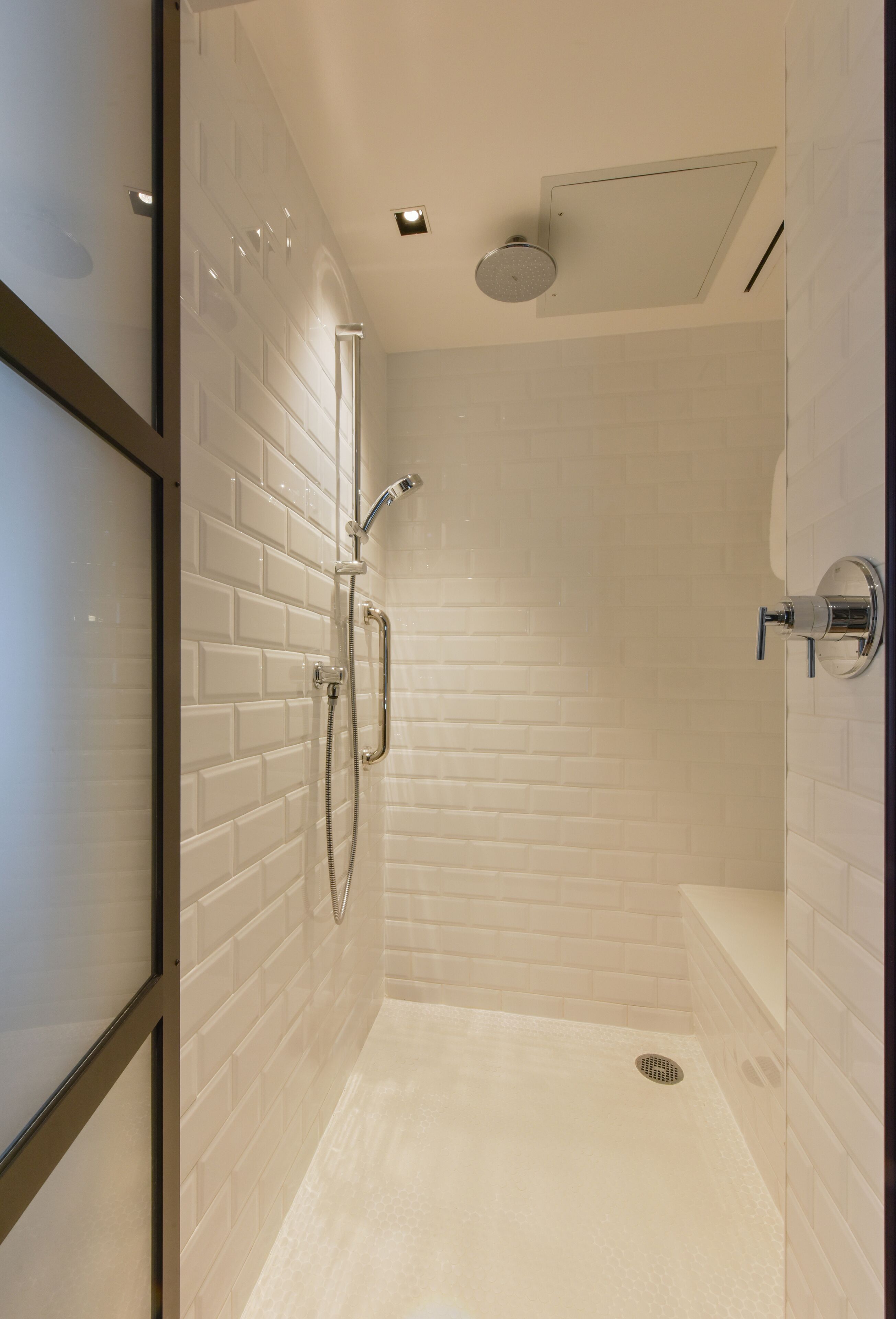 A modern shower with white tiled walls and a glass door.
