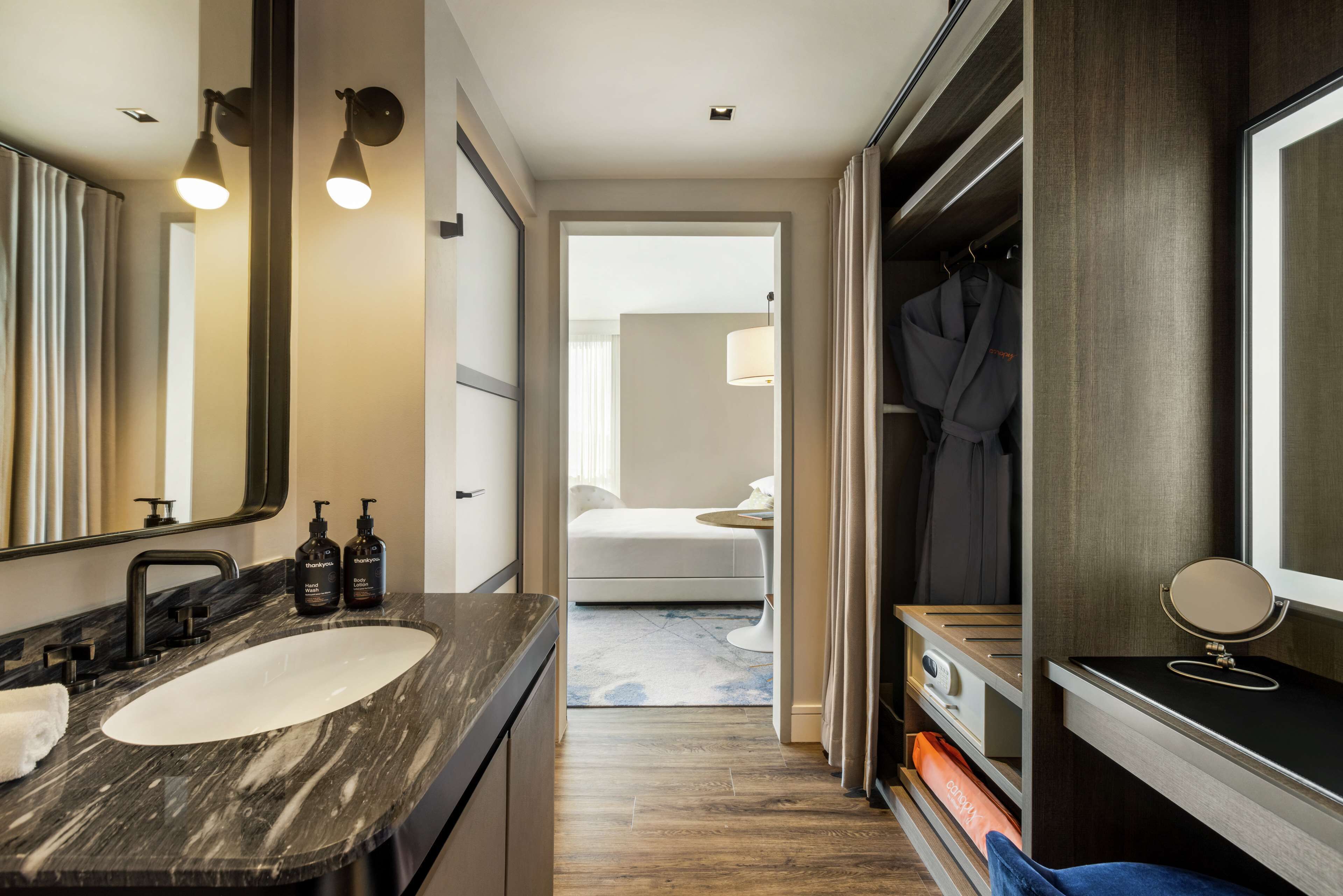 A modern bathroom with a marble sink, dark wood vanity, and a walk-in closet with a mirror and robe.