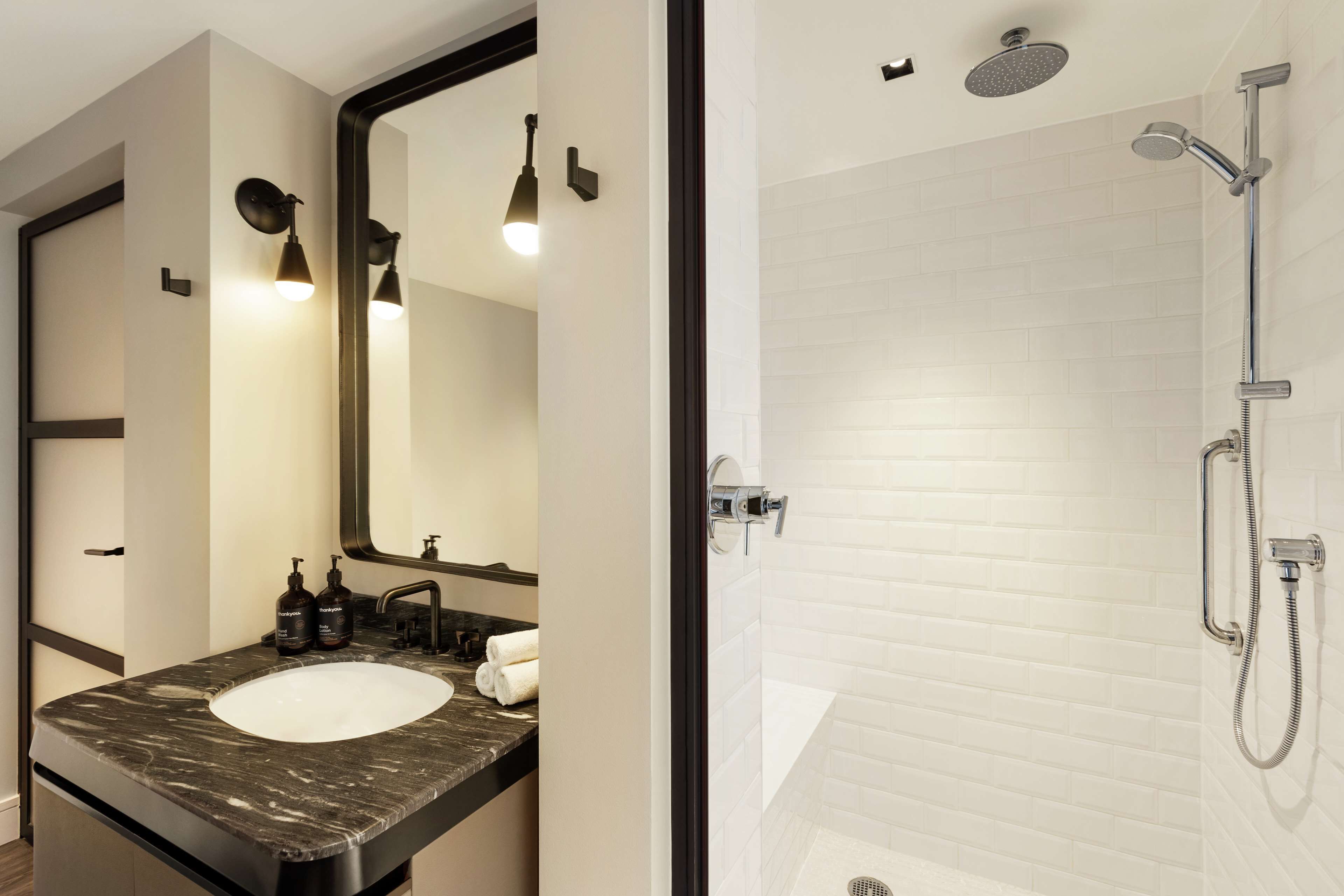 A bathroom with a marble sink, a large mirror, and a shower with a handheld showerhead.