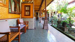 A covered corridor with wooden benches and a tiled floor, leading to a garden area with potted plants and a statue. - Bamboo Inn Kuta (Kuta)