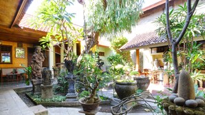 A courtyard with stone statues, potted plants, and a tiled-roof building. - Bamboo Inn Kuta (Kuta)