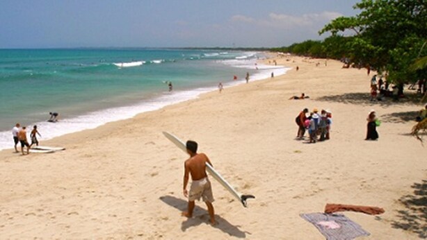 A beach with people, a surfboard, and a flag. - Bamboo Inn Kuta (Kuta)