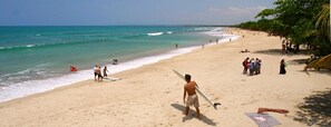A beach with people, a surfboard, and a flag. - Bamboo Inn Kuta (Kuta)