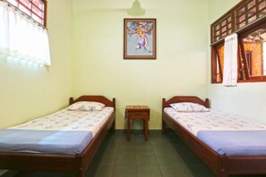 A room with two wooden beds, a small table, and a framed picture on the wall. - Bamboo Inn Kuta (Kuta)