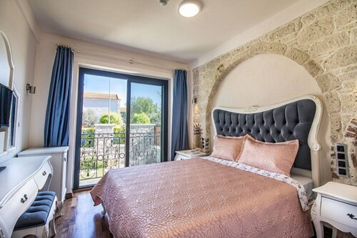 A bedroom with a large bed, a nightstand, a dresser, and a view of the outside balcony.