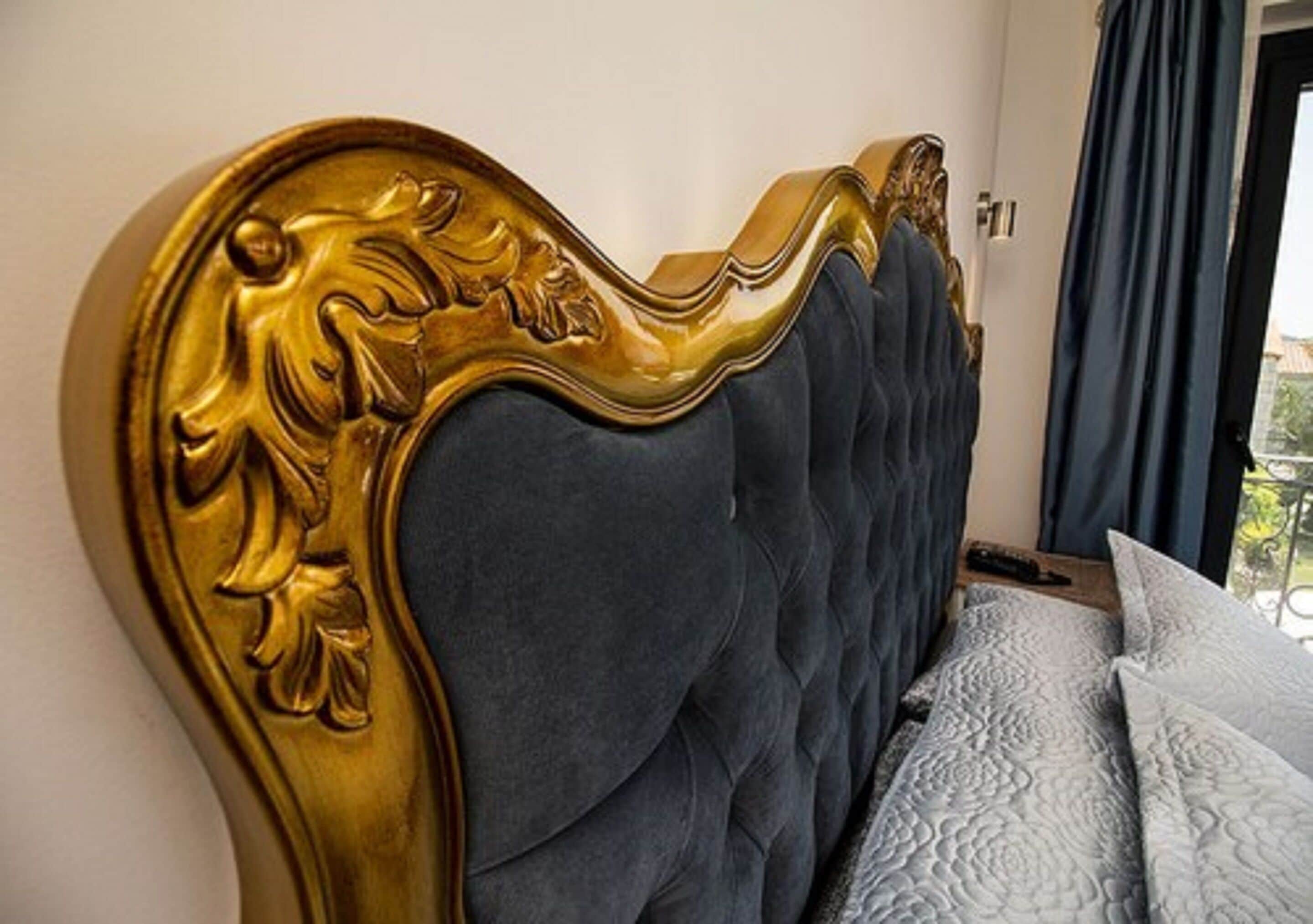 A bed with a dark headboard and a decorative gold frame.
