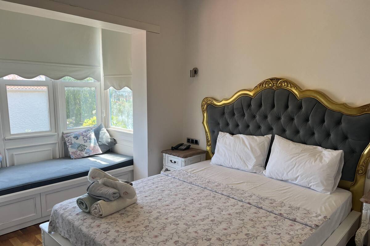 A bedroom with a large bed, a window seat, a bedside table, and a nightstand.