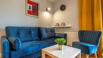Een woonkamer met een blauwe bank, een witte salontafel en een donker fauteuil.