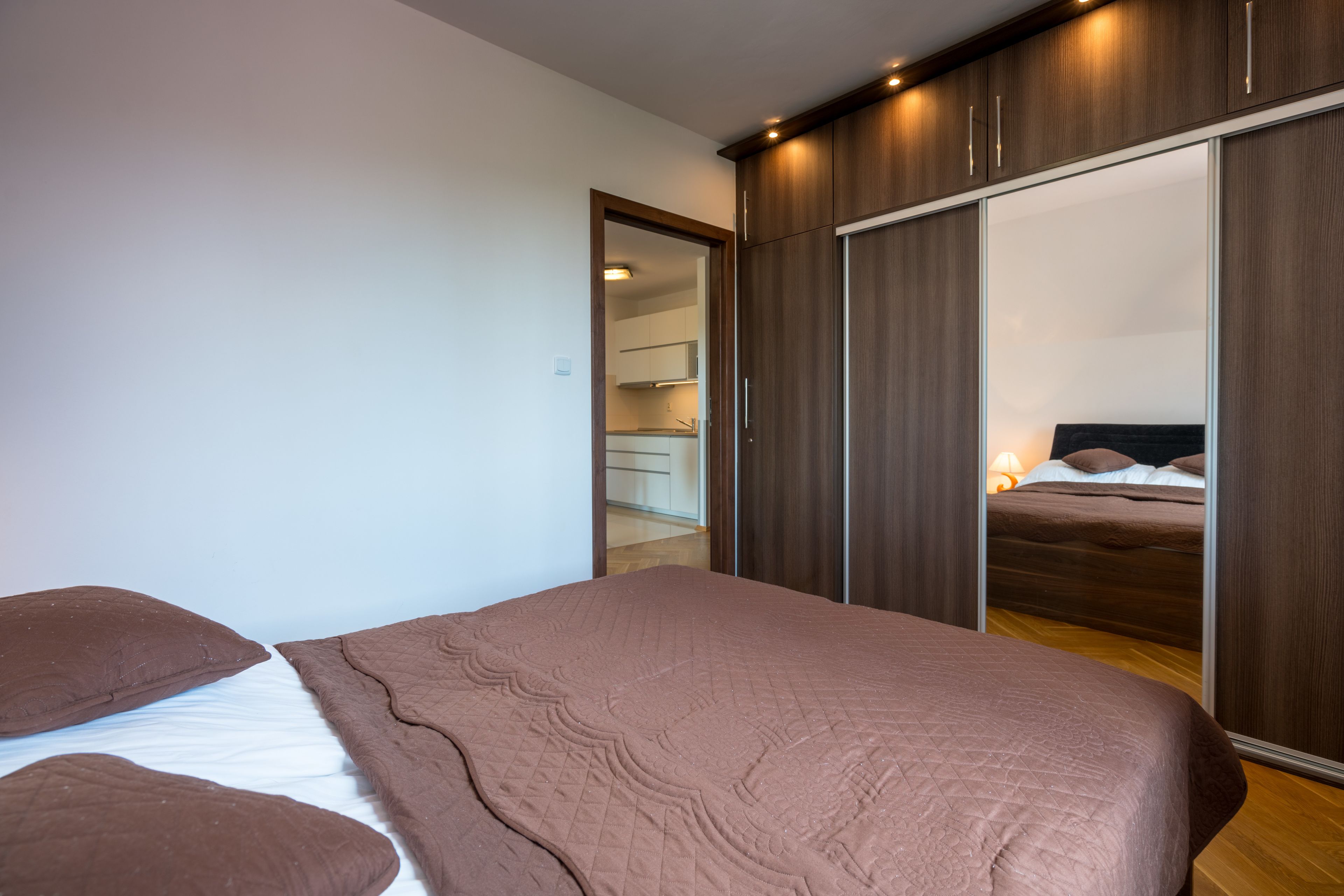 A bedroom with a large bed, a wardrobe with sliding doors, and a mirror reflecting the room.