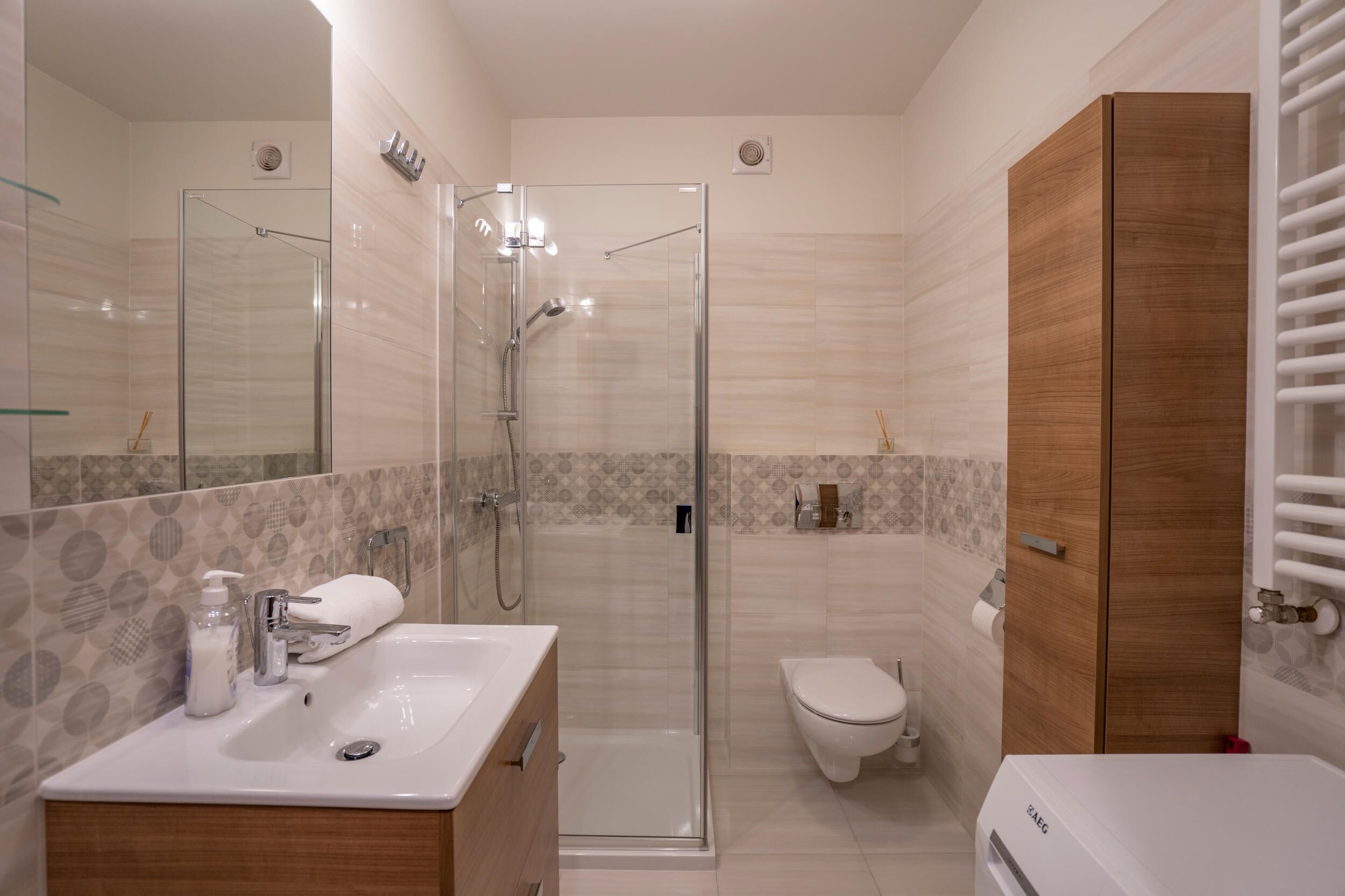 A modern bathroom with a glass-enclosed shower, a wooden vanity, a toilet, and a built-in heater.