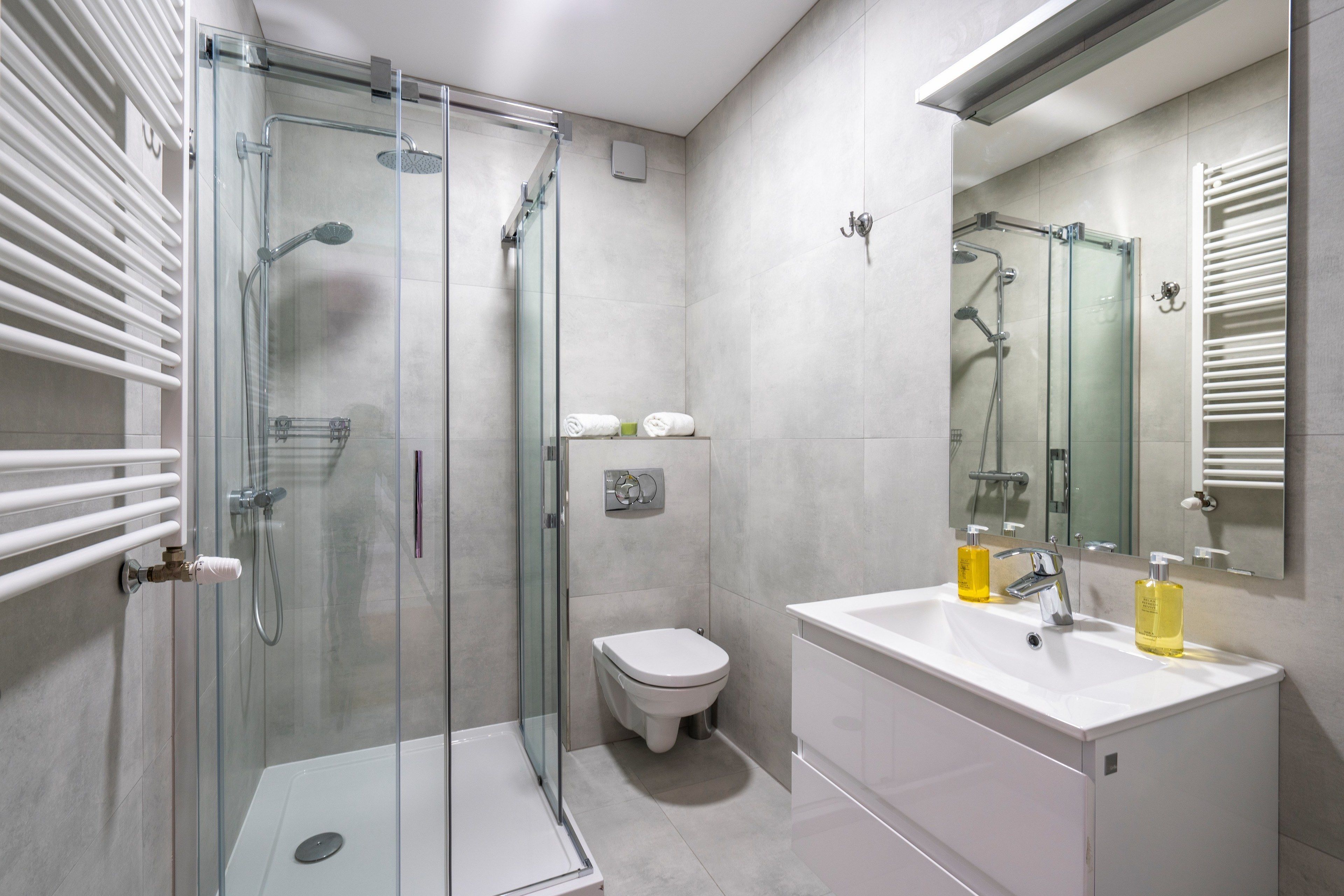 Un bagno moderno con cabina doccia in vetro, un lavandino bianco con due flaconi di sapone e un water.