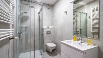 Un bagno moderno con cabina doccia in vetro, un lavandino bianco con due flaconi di sapone e un water.
