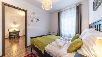 A bedroom with a bed, green pillows, a wooden headboard, a red rug, a wall clock, and a dining area with a table and chairs.