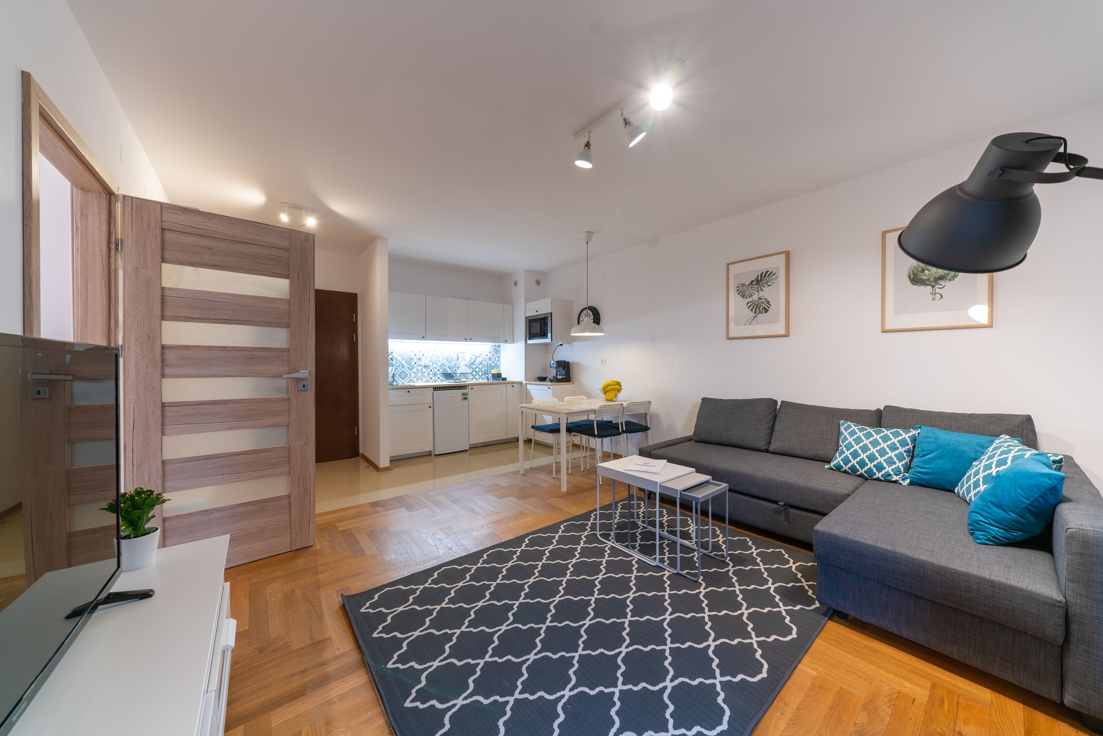 A modern living room with a grey sofa, a black and white rug, and a wooden door.