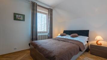A bedroom with a bed, a nightstand, a lamp, a window with curtains, and a framed picture on the wall.