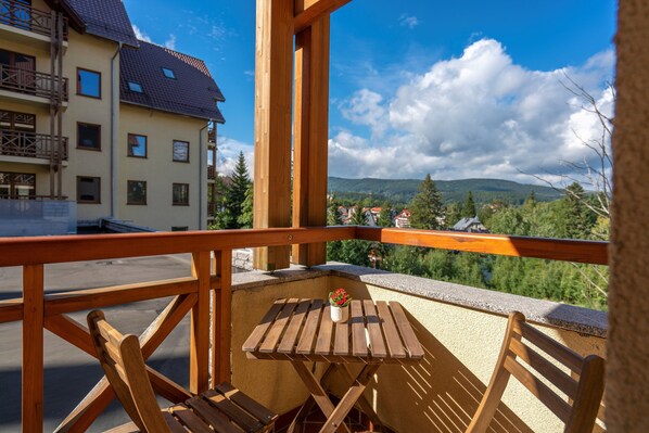 Un balcón con mesa y sillas de madera, una planta en maceta y vistas a un pueblo y montañas.