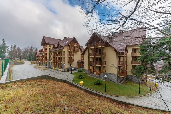 A row of chalet-style buildings with balconies, a paved driveway, and a grassy area with a small pond. - RentPlanet - Apartamenty Urocza (Szklarska Poreba)