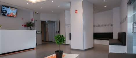 A modern reception area with a white reception desk, a potted plant, and a seating area with a black bench.