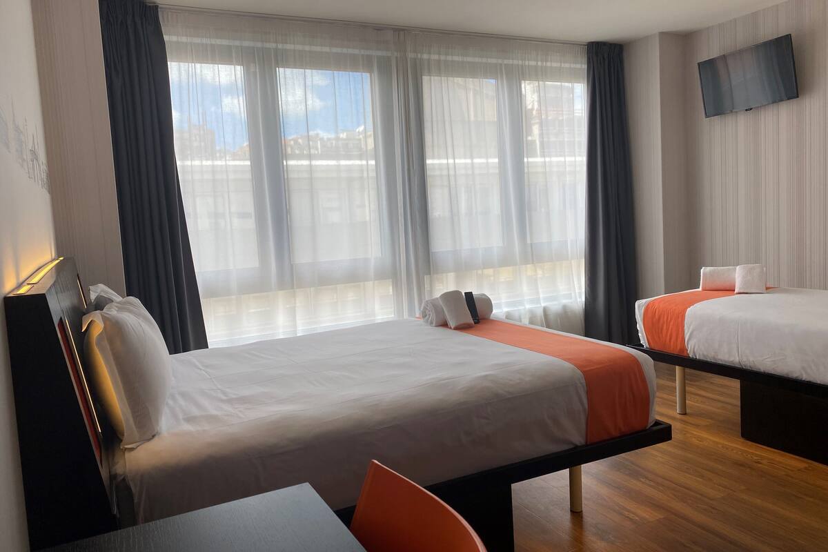 Une chambre d’hôtel avec deux lits, un téléviseur fixé au mur et une vue sur la ville grâce à de grandes fenêtres.
