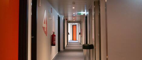 A hotel corridor with a fire extinguisher, a trash bin, and an exit sign.
