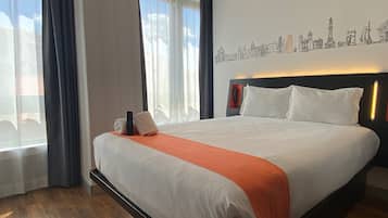 Quarto de hotel com uma cama grande, arte de parede com paisagem urbana e vista para o exterior pela janela.